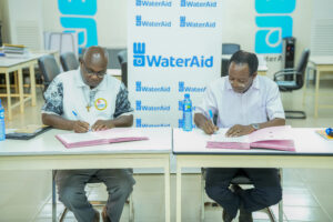 Two men signing documents at a table in front of a WaterAid branded backdrop.