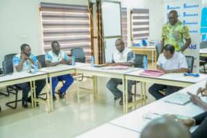Five men sit around a conference table in a bright room, some taking notes, WaterAid banners in the background.
