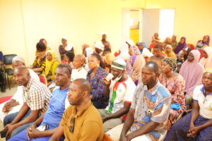 A diverse group of men and women seated in a crowded room at a community event or meeting.